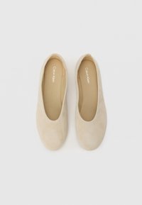 Beige Wildleder Ballerinas mit runder Spitze, glatter Textur und minimaler Naht. Logo "Calvin Klein" in Weiß auf der Innensohle gedruckt.
