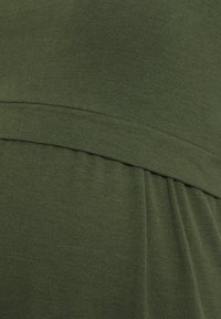 Close-up of olive green fabric with gathered seam detail on a soft, stretchy material.