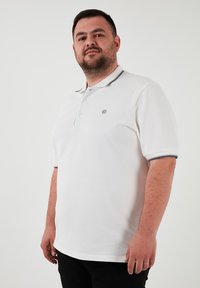 Biela polo košeľa z textúrovanej tkaniny, s šedým golierom a akcentmi, s rázporkom na tri gombíky a malým vyšitým logom na hrudi.
