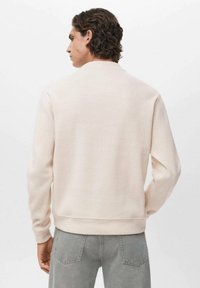 Sudadera de cuello redondo en color rosa claro, hecha de un tejido suave. Presenta puños y dobladillo acanalados, con un acabado texturizado. Sin marcas ni patrones visibles.