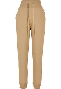Beige joggebukser laget av mykt stoff; har elastisk midje med snøring, sidelommer og innsnevrede mansjetter.