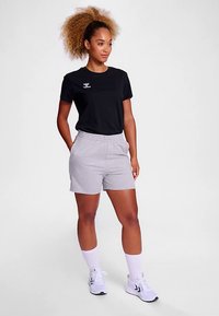 Μαύρο κοντομάνικο μπλουζάκι με λογότυπο, συνδυασμένο με ανοιχτό γκρι σορτς με ελαστική μέση. Το μοντέλο φοράει λευκές κάλτσες και αθλητικά παπούτσια.