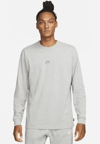 Pikend käistega hall dressipluus, mis on valmistatud pehmest kangast, millel on rinnal väike tikandiga Nike logo ja soonikkoes mansetid.