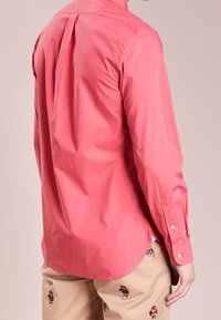 Korálová košile na knoflíky se sklady na zadní straně, dlouhými rukávy a hladkou, lehkou texturou. Přizpůsobený střih s zaobleným lemem.