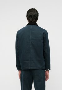 Chaqueta azul oscura con un cuello negro en contraste, de corte recto y puños abotonados. Tejido suave con textura mínima.