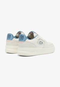Baskets blanches avec tige en daim et cuir, accents bleu clair, col rembourré, bout rond et semelle en caoutchouc texturée. Présente le logo Lacoste sur le côté.