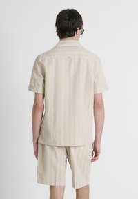 Camisa de manga corta, color Beige claro, con rayas verticales, tela texturizada y dobladillo recto. Combinada con pantalones cortos a juego.