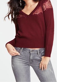 Burgundin neulepaita V-pääntiellä, jossa on pitsikoristeet harteilla, yhdistettynä vaaleanharmaisiin kulutettuihin farkkuihin.