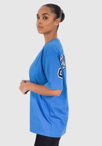 Camiseta azul de manga corta con escote redondo y diseño de texto negro en la parte posterior. Tela suave con un corte relajado.