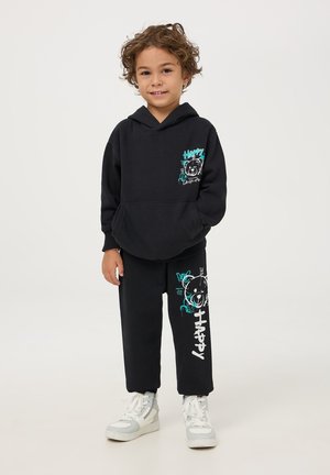 Czarny komplet z bluzą z kapturem i spodniami, z grafiką misia oraz napisem "HAPPY" w kolorze turkusowym i białym. Wykonany z miękkiego, wygodnego materiału. Białe trampki.