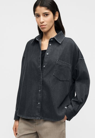Πουκάμισο από σκούρο τζιν με άνετη γραμμή, κουμπιά μπροστά, τσέπη στο στήθος και διακριτικές ραφές. Συνδυασμένο με ανοιχτόχρωμο παντελόνι.