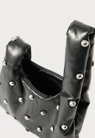 Bolsa de couro preta com um design acolchoado e pinos de metal prateados. Apresenta duas alças curtas e um topo aberto, exibindo o interior.