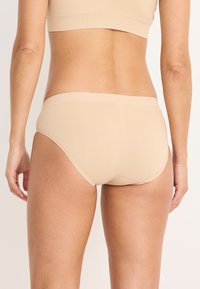 Beige sömlös underkläder med låg midja, slät textur och minimal detaljer. Har en mjuk elastisk midjeband.