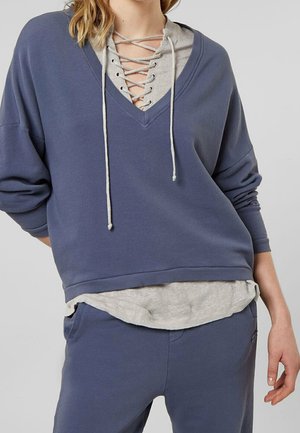 Oversized blauw sweatshirt met een V-hals en een grijs gelaagd shirt, met veterdetails en trekkoorden. Zachte stof met lange mouwen.