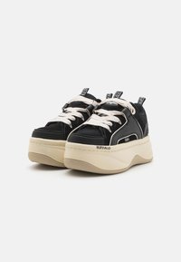 Svarte plattformsneakers med hvite snører, strukturert stoff og gummisåler. Har kontrasterende svart og beige design samt merkevaredetaljer.