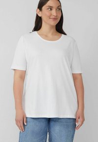 Weißes T-Shirt mit kurzen Ärmeln und rundem Halsausschnitt, aus weichem Stoff; lässiger Schnitt und glatte Textur. Getragen mit hellblauen Jeans.