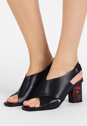 Zwarte leren open teen haksandalen met een kruiselings ontwerp, vierkante neus en een blokhak met een schildpadpatroon. Bevat een metalen accent.