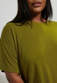 Grünes Kurzarmoberteil mit lockerer Passform, Rundhalsausschnitt und subtiler strukturiertem Stoff, das ein einfaches, sauberes Design präsentiert.