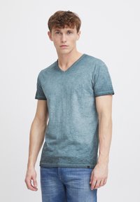Camisa de T-shirt de cuello en V de color azul claro, hecha de una tela mezclada con una sutil textura, combinada con jeans azules. Mangas cortas y dobladillo recto.