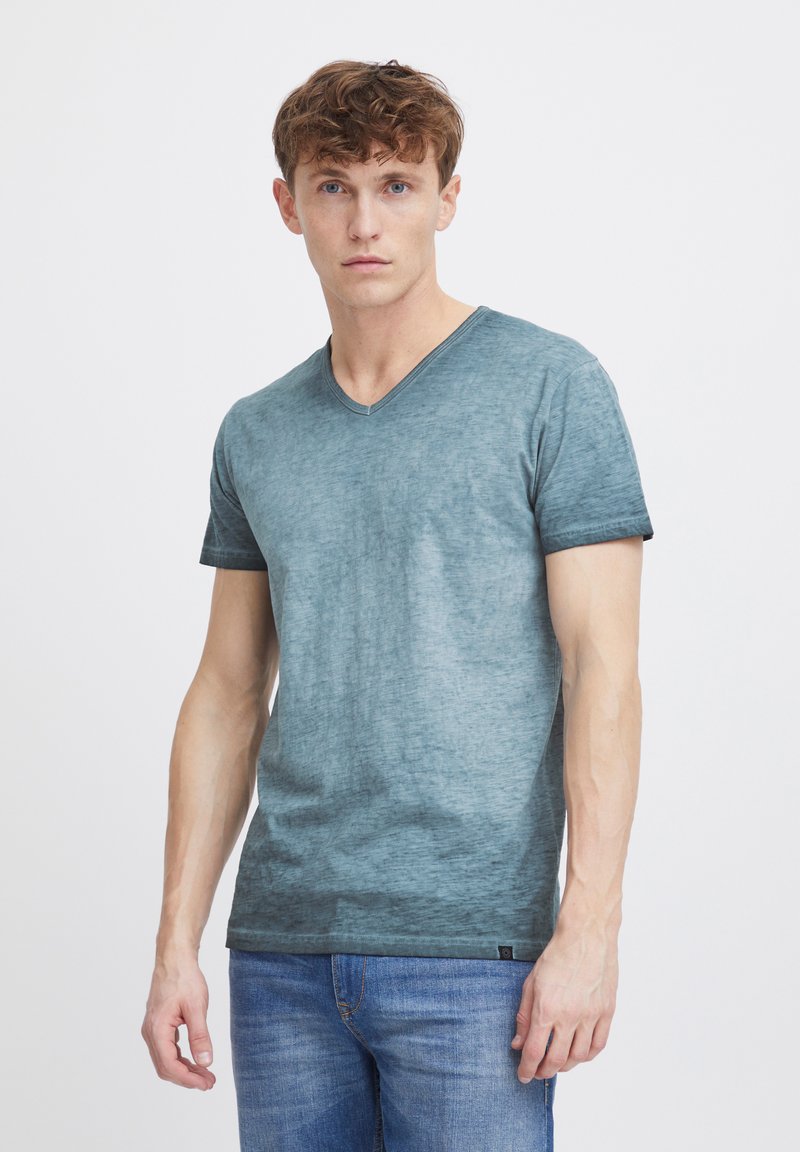 Camisa de T-shirt de cuello en V de color azul claro, hecha de una tela mezclada con una sutil textura, combinada con jeans azules. Mangas cortas y dobladillo recto.