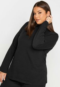 Svart långärmad turtleneck-tröja gjord av mjukt tyg, med en avslappnad passform och minimala sömmar för komfort. Slät yta och enkel design.