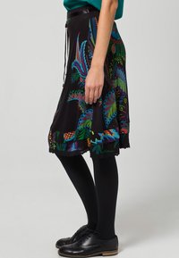Czarna spódnica z kolorowymi wzorami kwiatów i liści. Wykończona falbaniastym dołem, noszona z czarnymi rajstopami i sznurowanymi butami.