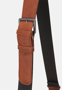 Brązowy skórzany pasek z czarną tkaniną, z metalową klamrą w kolorze srebrnym i przeszyciami, odpowiedni do regulacji dopasowania.