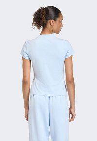 Svetlomodré tričko s krátkym rukávom a priliehavým strihom. Hladký povrch, okrúhly výstrih a skromná dĺžka. V kombinácii so zodpovedajúcimi svetlomodrými nohavicami.
