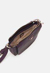 Fialová texturovaná kabelka se zipovým uzávěrem a zlatými kovovými doplňky. Interiér je světle béžový s logem značky a má odnímatelný popruh.