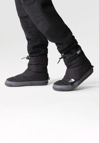Botas aisladas negras con acabado texturizado, que cuentan con suela de goma, cordón ajustable y acentos de logotipo. Diseño compacto y resistente al agua.
