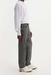 Sudadera gris claro, jeans oscuros grises holgados y zapatillas blancas con detalles verdes. Diseño sencillo, textura suave y corte relajado.