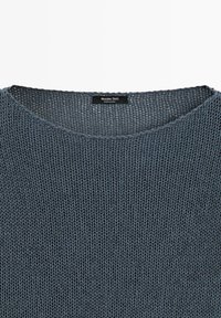 Maglione grigio scuro lavorato a maglia con scollo arrotondato e etichetta nera con la scritta "Massimo Dutti Made in China" all'interno del colletto.