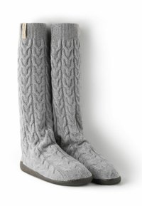 Szare dziergane ochraniacze na nogi z warkoczowym wzorem, miękką fakturą i płaską podeszwą. Zawierają małą metkę z logo na górnym brzegu.