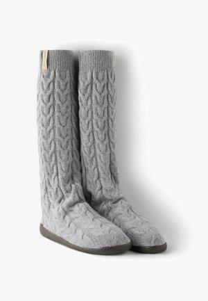 Graue, gestrickte Beinwärmer mit einem Zopfmuster, weicher Textur und flachen Sohlen. Mit einem kleinen Logotag am oberen Rand versehen.