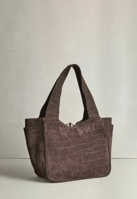 Pruun seemisnahast kübarakott krokodillinahkse mustriga, laiad sangad ja ümar põhjaga, asetatud helele neutraalsele pinnale.