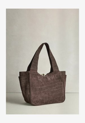 Pruun seemisnahast kübarakott krokodillinahkse mustriga, laiad sangad ja ümar põhjaga, asetatud helele neutraalsele pinnale.