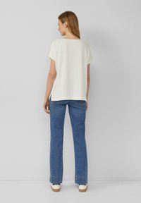 Witte T-shirt met korte mouwen in een gestructureerde, losse pasvorm, gecombineerd met lichtblauwe flared jeans en witte sneakers met tan accenten.