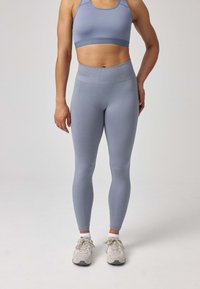 Completo sportivo azzurro chiaro composto da un reggiseno sportivo aderente e leggings a vita alta. Textura morbida, design senza cuciture, abbinato a sneakers grigio chiaro.