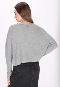Szary, oversize sweter z dzianiny o luźnym kroju, z ribbowanym dołem i luźnymi rękawami. Połączony z czarną spódnicą z wysokim stanem z denimu.