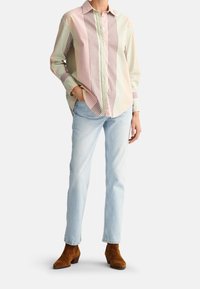 Chemise à rayures avec des teintes rose, vert et marron, associée à un jean bleu clair et des bottines en suède marron. Coupe décontractée, manches longues.