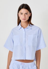 Camicia corta a maniche corte a righe bianche e azzurre, con due tasche applicate frontali, chiusura con bottoni e colletto.