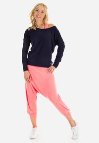 Granatowa bluza bez ramion i różowe spodnie haremowe wykonane z miękkiego materiału, uzupełnione białymi trampkami, tworzące swobodny, sportowy wygląd.