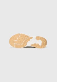 Sål af en sneaker med en fleksibel hvid mellemsål og en tekstureret gummiydersål i lys brun, med dækmønstre for greb.