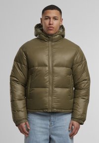 Olíva zöld pufikabát kapucnival, fényes sima textúrával, cipzáras elülső záródással és rugalmas mandzsettákkal, semleges háttér előtt.