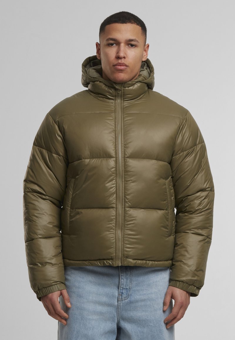 Olíva zöld pufikabát kapucnival, fényes sima textúrával, cipzáras elülső záródással és rugalmas mandzsettákkal, semleges háttér előtt.