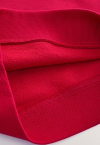 Punane dressipluus, millel on pehme, fliisilaadne sisevooder ja soonikkoes mansetid. Sile tekstuur ning korralikud õmblused mööda servi.