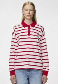 Camisa polo de manga larga en blanco con rayas horizontales rojas, con un cuello rojo y una tapeta de tres botones. Tejido de algodón, corte relajado.