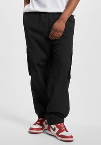 Schwarze Cargo-Hosen mit elastischem Bund, Seitentaschen und schmal zulaufenden Bündchen, kombiniert mit rot-weißen Sneakers. Glattes, leichtes Material.