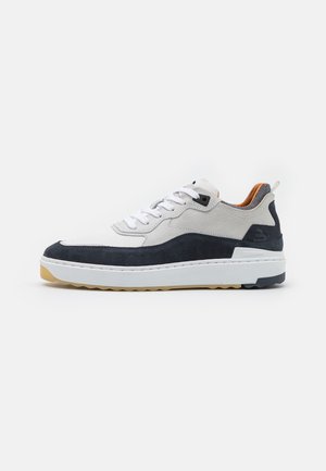 Sneakers featuring a white mesh upper, navy blue suede accents, a gum rubber outsole, and white laces. Notable stitching detail along the sole.
