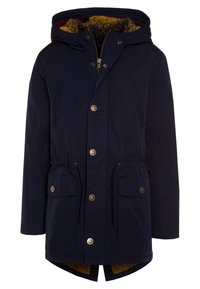 Námořnická voděodolná parka s kapucí podšitou umělou kožešinou, se zipovým zapínáním a stahovacími šňůrkami v pase. Obsahuje zlaté knoflíky a dvě přední kapsy.